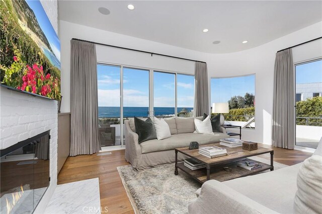 living room with a water view, a brick fireplace, and light hardwood / wood-style floors