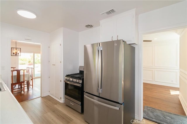 kitchen with an inviting chandelier, white cabinets, stainless steel appliances, and light wood-type flooring