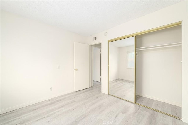 unfurnished bedroom featuring light hardwood / wood-style flooring, a closet, and a textured ceiling