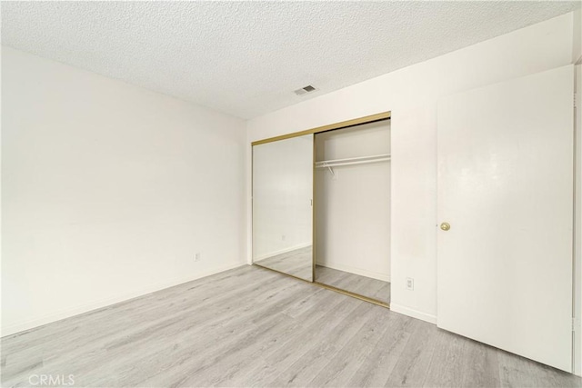 unfurnished bedroom with a textured ceiling, light wood-type flooring, and a closet