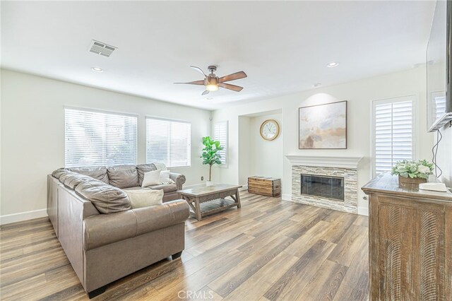 living room featuring ceiling fan, hardwood / wood-style floors, and a stone fireplace