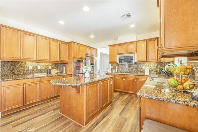 kitchen featuring appliances with stainless steel finishes, light wood-type flooring, a kitchen island, a breakfast bar, and sink