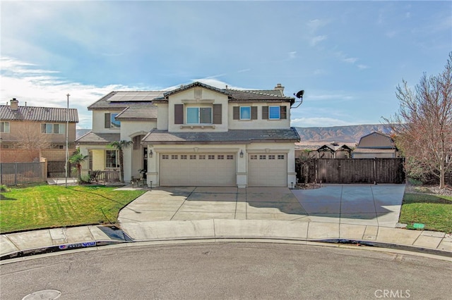 view of front of property with a garage, a mountain view, a front lawn, and solar panels