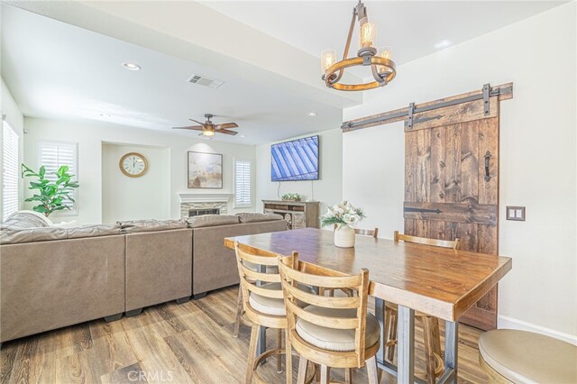 dining area featuring ceiling fan with notable chandelier, a healthy amount of sunlight, a barn door, and light hardwood / wood-style flooring