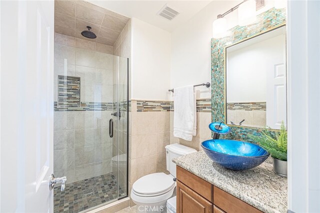 bathroom featuring toilet, vanity, tile walls, and a shower with door