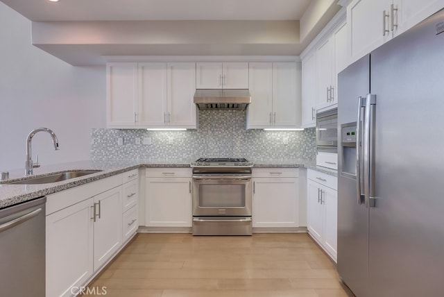 kitchen featuring backsplash, wall chimney range hood, sink, stainless steel appliances, and white cabinets