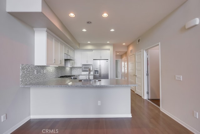 kitchen with kitchen peninsula, stainless steel refrigerator with ice dispenser, sink, white microwave, and white cabinets