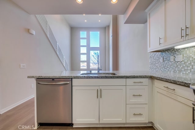 kitchen with light stone countertops, white cabinets, dishwasher, and kitchen peninsula