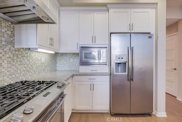 kitchen with tasteful backsplash, white cabinets, stainless steel appliances, and range hood