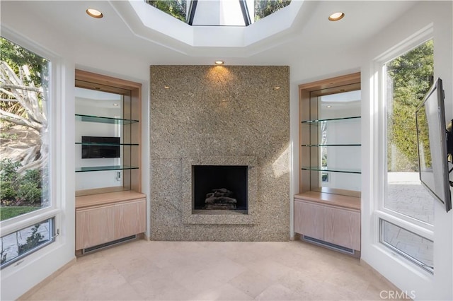 unfurnished living room featuring a raised ceiling, a fireplace, a skylight, and recessed lighting