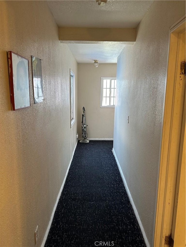 hallway with beam ceiling, a textured ceiling, and carpet flooring