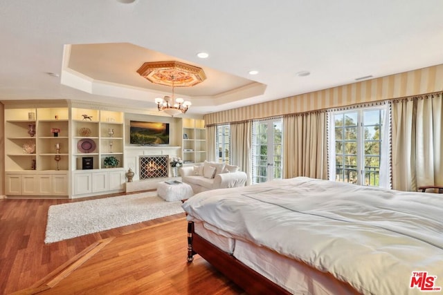 bedroom with access to outside, an inviting chandelier, a tray ceiling, and hardwood / wood-style floors