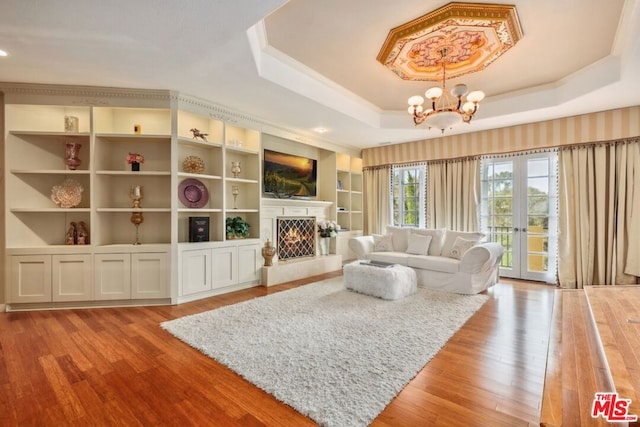 living room featuring a raised ceiling, french doors, a chandelier, light hardwood / wood-style flooring, and built in shelves