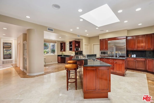 kitchen with a skylight, backsplash, a kitchen breakfast bar, built in appliances, and a center island