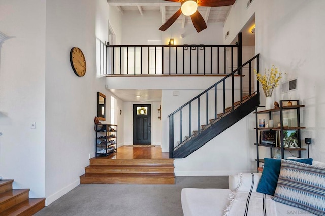 stairs featuring a high ceiling, beam ceiling, ceiling fan, and concrete floors