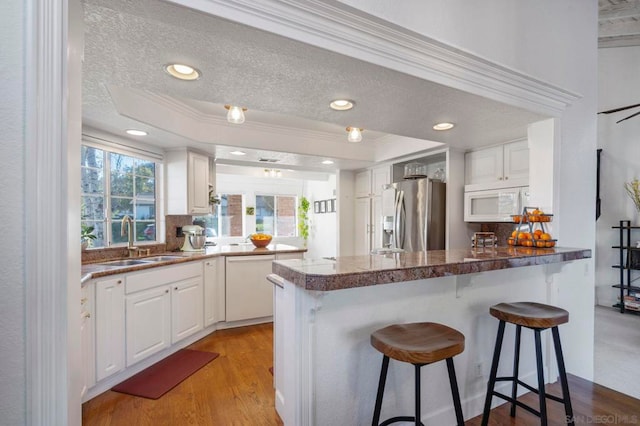 kitchen with sink, white appliances, white cabinetry, and kitchen peninsula