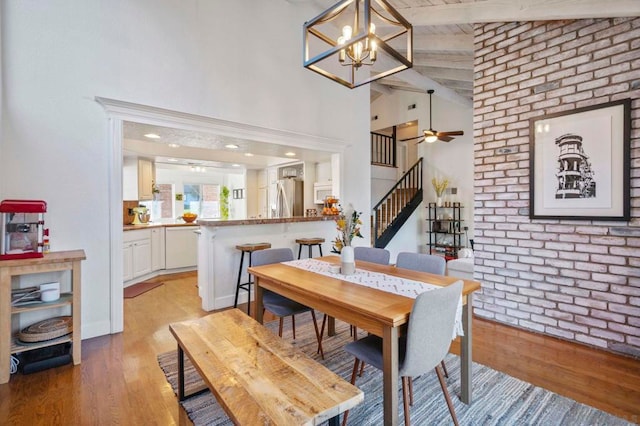 dining room with light hardwood / wood-style flooring, brick wall, high vaulted ceiling, beam ceiling, and ceiling fan with notable chandelier