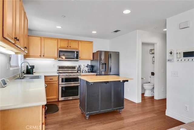 kitchen with appliances with stainless steel finishes, light hardwood / wood-style floors, a center island, sink, and butcher block counters