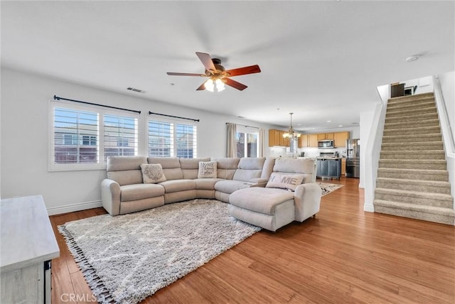 living room with light wood-type flooring and ceiling fan with notable chandelier