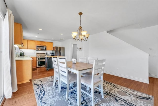 dining space with sink, light wood-type flooring, and an inviting chandelier