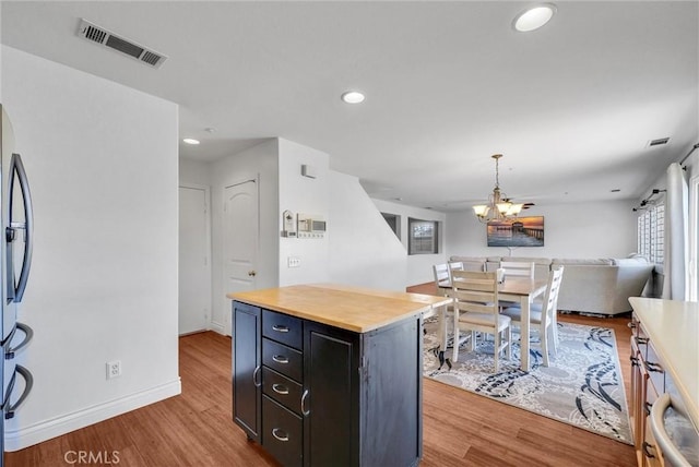 kitchen with light hardwood / wood-style flooring, pendant lighting, a notable chandelier, stainless steel fridge, and a kitchen island