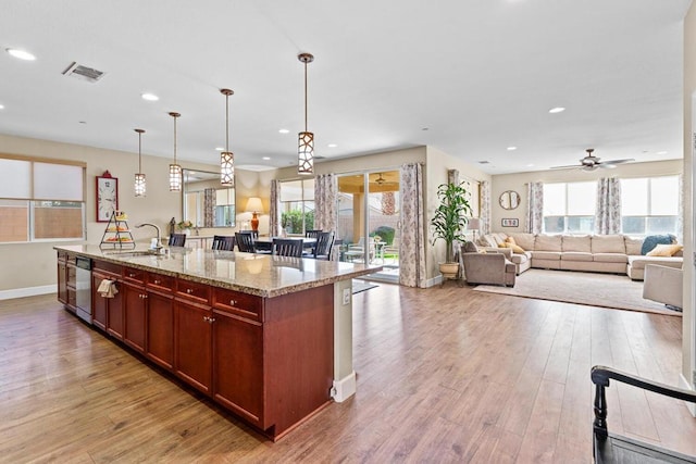 kitchen with pendant lighting, an island with sink, sink, light stone countertops, and light hardwood / wood-style flooring