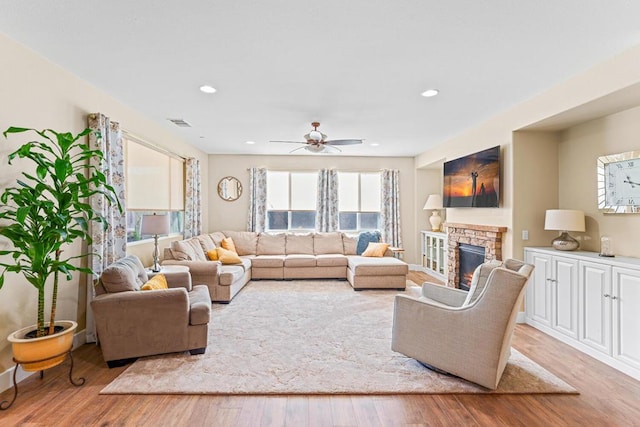 living room featuring ceiling fan, a fireplace, and light wood-type flooring