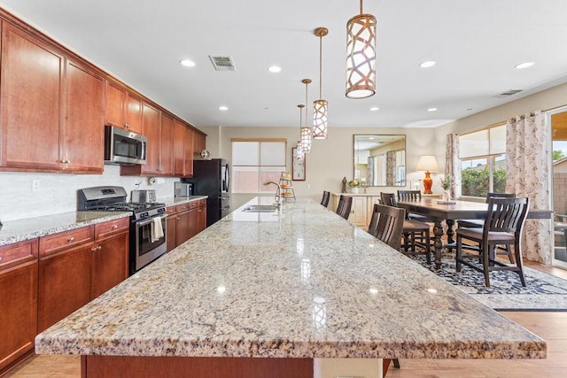 kitchen featuring pendant lighting, sink, stainless steel appliances, and a large island with sink