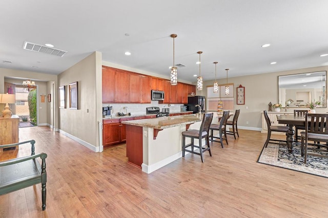 kitchen with a breakfast bar, light stone counters, decorative light fixtures, appliances with stainless steel finishes, and a kitchen island with sink