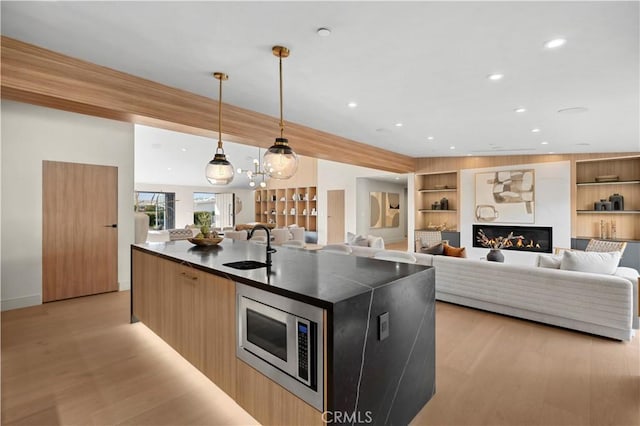 kitchen with sink, hanging light fixtures, stainless steel microwave, built in features, and a kitchen island with sink