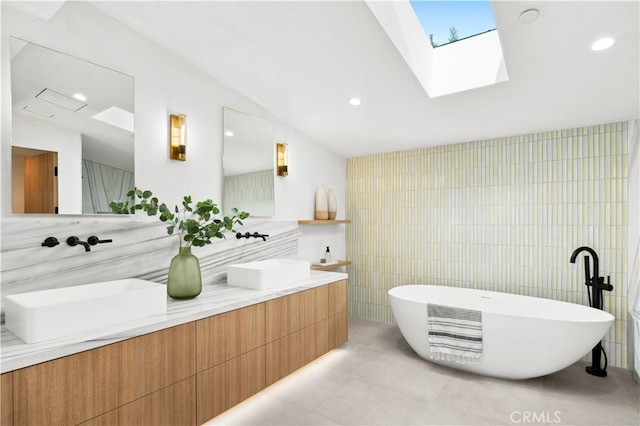 full bath with double vanity, tile walls, a soaking tub, a sink, and a skylight