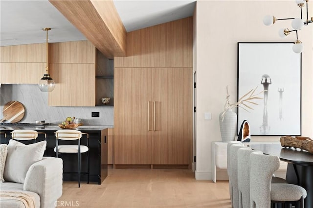 kitchen with tasteful backsplash, light brown cabinetry, hanging light fixtures, and light wood-type flooring