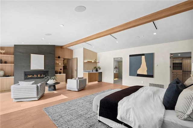 bedroom with vaulted ceiling with beams, a large fireplace, and light wood-type flooring