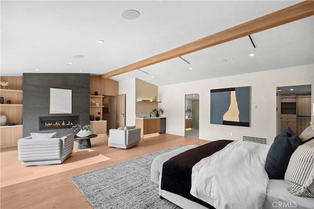 bedroom with light wood-style floors, vaulted ceiling with beams, a fireplace, and visible vents
