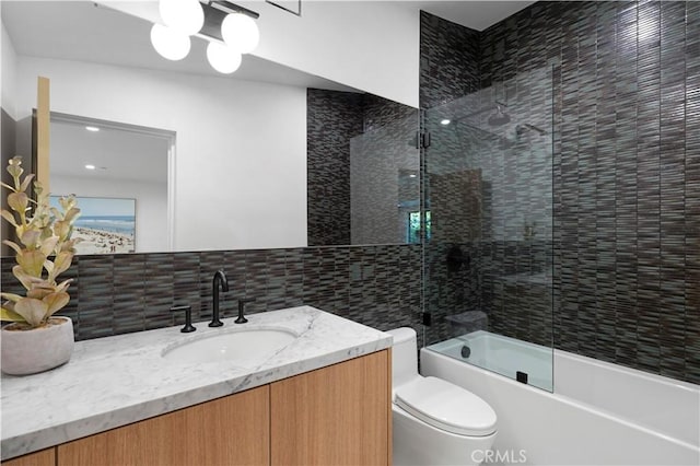 bathroom featuring vanity, decorative backsplash, shower / bath combination with glass door, toilet, and tile walls