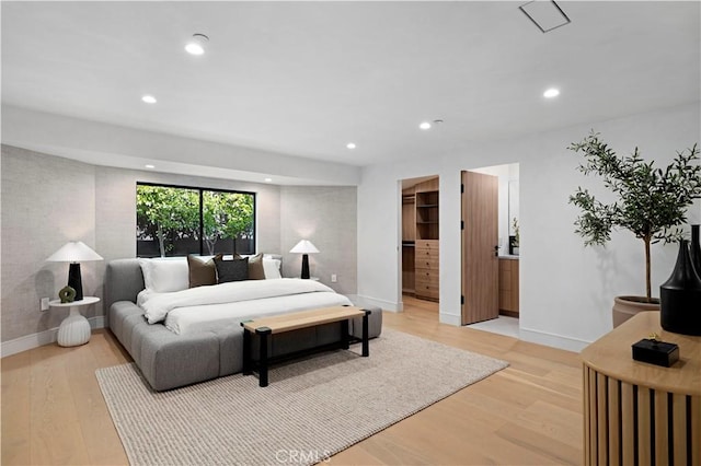 bedroom featuring a walk in closet, connected bathroom, a closet, and light wood-type flooring