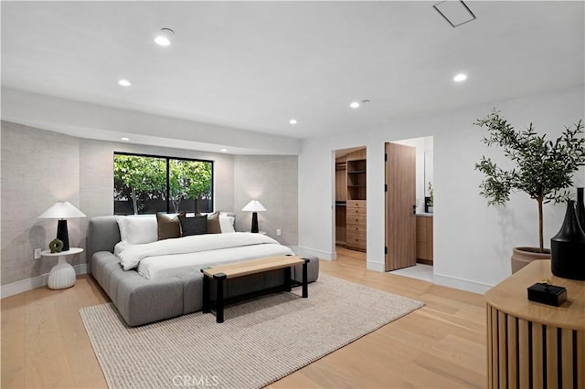 bedroom featuring light wood-style floors, baseboards, recessed lighting, and a walk in closet