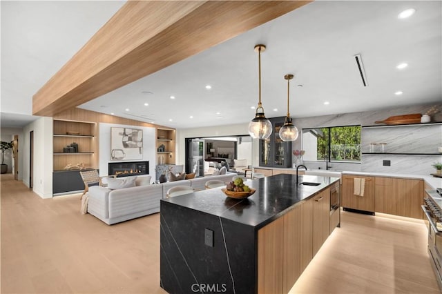 kitchen featuring stainless steel microwave, decorative light fixtures, sink, a large island, and light hardwood / wood-style floors