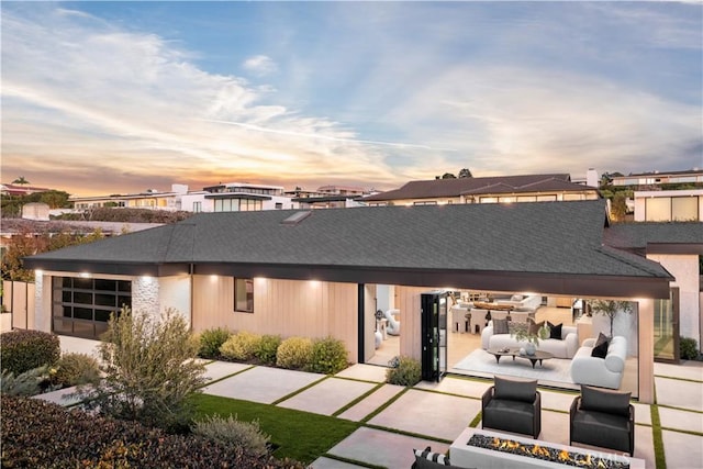 rear view of property with an outdoor living space with a fire pit, an attached garage, and a patio area