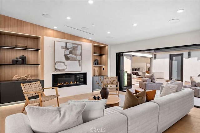 living area with recessed lighting, built in features, a glass covered fireplace, and wood finished floors