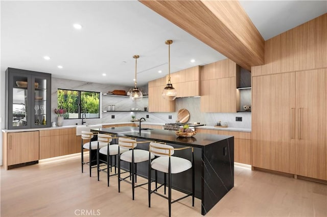 kitchen featuring light brown cabinetry, tasteful backsplash, an island with sink, sink, and hanging light fixtures