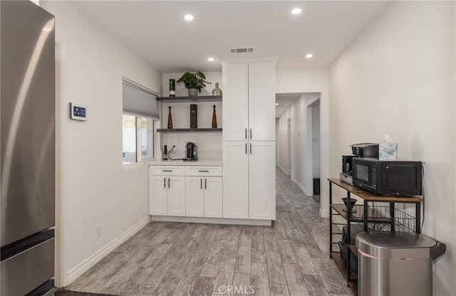 kitchen with light wood-type flooring, stainless steel fridge, and white cabinetry