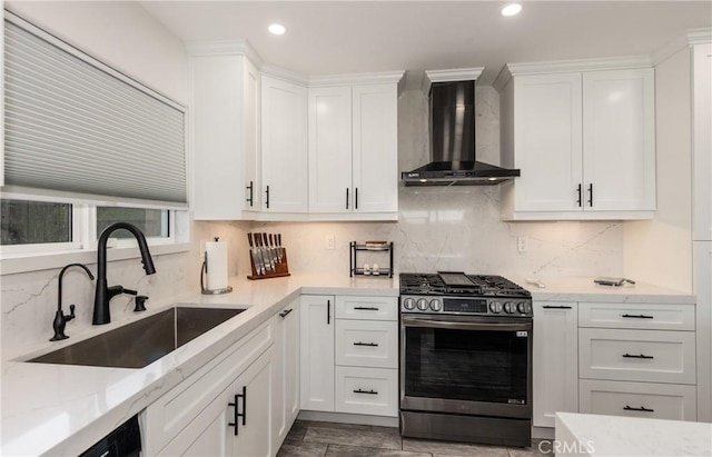 kitchen with wall chimney range hood, sink, white cabinetry, light stone countertops, and gas range