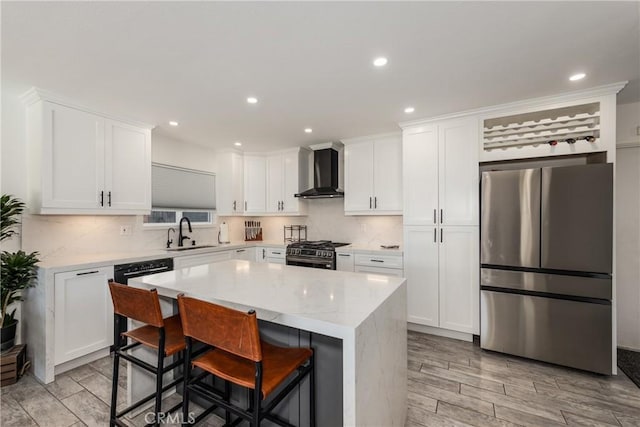 kitchen featuring appliances with stainless steel finishes, a kitchen island, wall chimney range hood, sink, and a kitchen breakfast bar