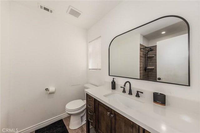 bathroom featuring wood-type flooring, toilet, vanity, and a tile shower