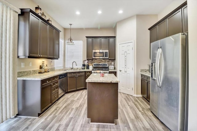 kitchen with pendant lighting, stainless steel appliances, a center island, and light wood-type flooring