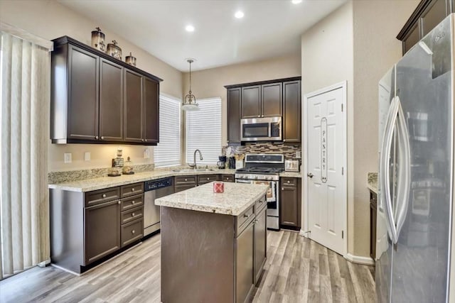 kitchen with sink, decorative light fixtures, a center island, appliances with stainless steel finishes, and light hardwood / wood-style floors