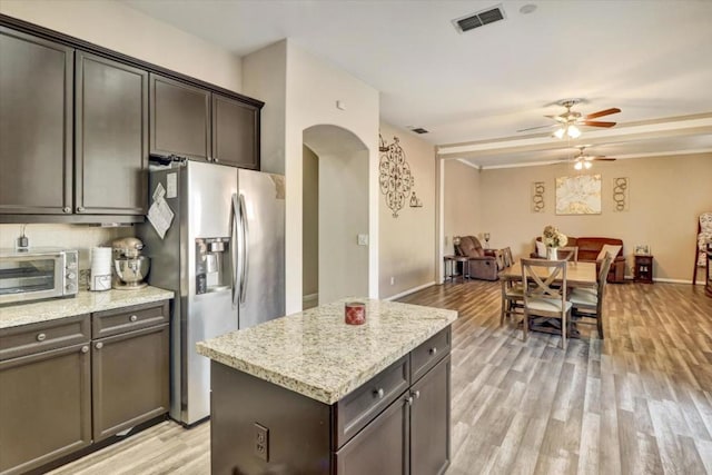 kitchen featuring stainless steel fridge with ice dispenser, a center island, light stone counters, ceiling fan, and light wood-type flooring