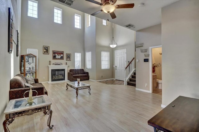 living room featuring ceiling fan, a high ceiling, and light wood-type flooring