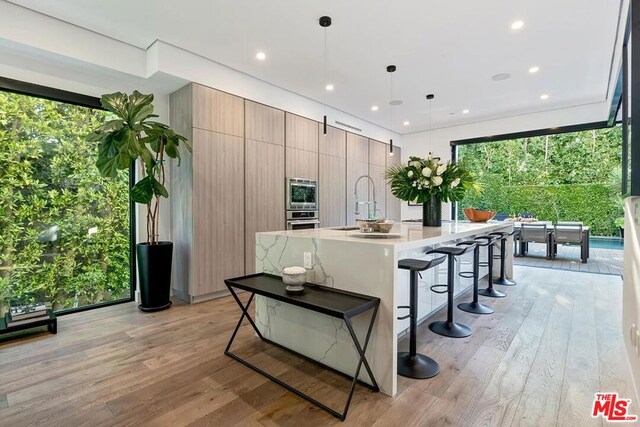 kitchen featuring appliances with stainless steel finishes, an island with sink, a kitchen breakfast bar, hanging light fixtures, and light hardwood / wood-style flooring